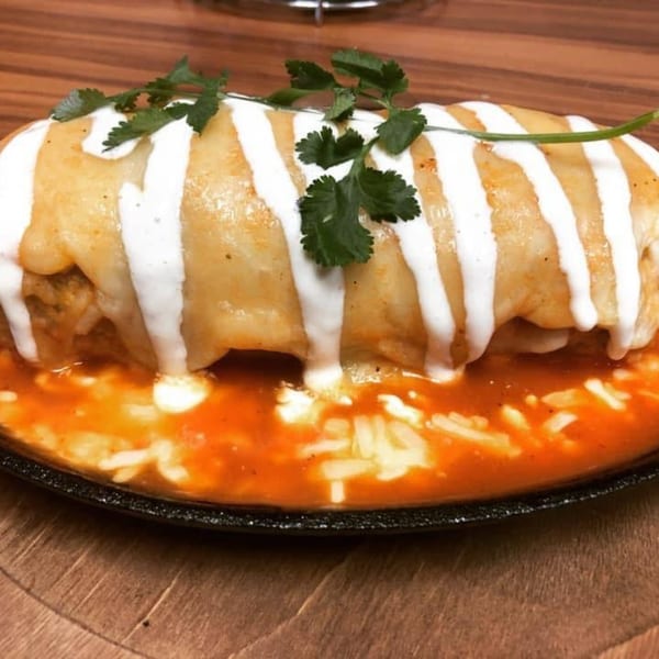 A large, smothered burrito with white sauce stripes and cilantro, sitting in a pool of red sauce.