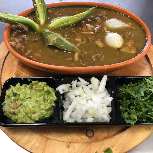 Mexican stew with whole peppers and onions, served with guacamole, diced onions, and cilantro.