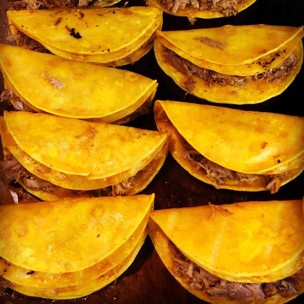 Close-up of several golden-fried tacos filled with shredded meat, cooking on a dark surface.
