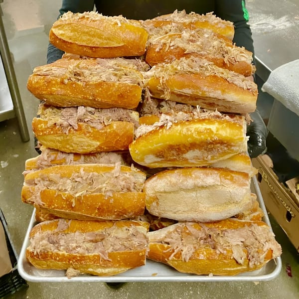 A person holds a large tray overflowing with many golden-brown tortas ahogadas, filled with shredded meat.